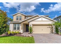 Charming two-story home with landscaped yard, tan siding, and a brick driveway under a sunny sky at 2335 Green Symphony Pl, Oviedo, FL 32765