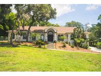 Charming single-story home with arched windows, landscaped yard, and mature trees at 16400 Lakeshore Dr, Minneola, FL 34715