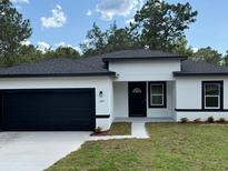A charming single-story home with a black garage door, white stucco, and a well-manicured lawn at 706 Marion Oaks Manor, Ocala, FL 34473