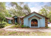 Charming single-story home featuring light blue siding, stone accents, arched window, and mature trees at 4933 Round Lake Rd, Apopka, FL 32712