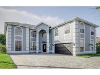 Spacious two-story home with an elegant grey exterior, large windows, and a patterned brick driveway at 224 Hammock Dunes Pl, Orlando, FL 32828