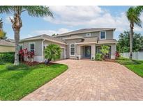Beautiful two-story home with manicured lawn, a brick driveway, and lush tropical landscaping at 15318 Sandfield Loop, Winter Garden, FL 34787