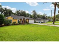 Charming yellow house featuring a well-manicured lawn, lovely landscaping, and an attached two-car garage at 395 Alcazar Ave, De Leon Springs, FL 32130