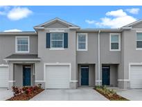Townhome exterior with grey facade, blue door and shutters, white garage door, and meticulously manicured landscaping at 712 Preston Cove Dr, St Cloud, FL 34771