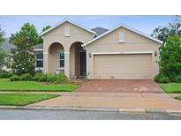 Charming beige home featuring a brick driveway, arched entryway, and well-maintained landscaping at 2339 Jernigan Loop, Kissimmee, FL 34746