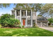 Classic two-story home boasts stately pillars, a well-manicured lawn, an orange front door, and mature landscaping at 11425 Claymont Cir, Windermere, FL 34786