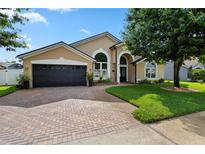 Charming tan home with a two-car garage, arched windows, and a brick driveway and walkway at 1008 Soldier Creek Ct, Oviedo, FL 32765
