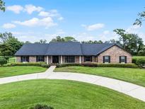 Charming brick home with a circular driveway, lush green lawn, and mature landscaping at 104 Amberwood Ct, Longwood, FL 32779