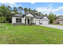 Charming single-story home featuring a two-car garage, well-maintained lawn, and modern architectural details at 136 N James Pl, Groveland, FL 34736