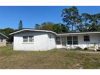 View of a one-story home with white cinderblock and a dark roof, with mature trees on the property at 115 Lake Dot Dr, Sanford, FL 32773