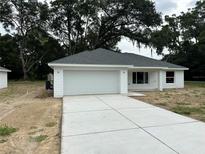 Charming one-story home features a gray roof, white siding, a concrete driveway and an attached two-car garage at 14495 Se 38Th Ter, Summerfield, FL 34491