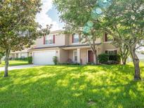Two-story home featuring a front lawn, a two-car garage, front porch, red shutters, and mature trees at 8330 Lainie Ln, Orlando, FL 32818