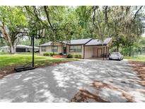 Charming single-story home featuring a large driveway, carport, and a well-manicured front yard shaded by mature trees at 1753 Nw 44Th St, Ocala, FL 34475