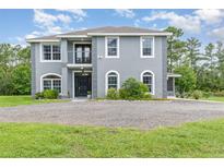 Two story home with grey stucco, manicured landscaping, black front door, and a circular gravel driveway at 32125 Wekiva Pines Blvd, Sorrento, FL 32776