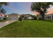 Charming single-story home featuring a lush green lawn, two car garage, and mature landscaping at dusk at 176 Hidden View Dr, Groveland, FL 34736