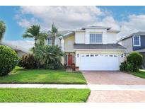 Charming two-story home with a well-manicured lawn, tropical plants, and a brick driveway at 2205 Wyndam Way, Kissimmee, FL 34743