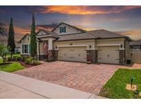 Charming home with a brick driveway, three-car garage, manicured lawn, and attractive landscaping under a colorful sunset sky at 5182 Appenine E Loop, St Cloud, FL 34771
