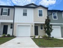 Two-story townhome featuring a one-car garage, nicely landscaped front yard, and neutral exterior paint at 497 Madison Dr, Davenport, FL 33837