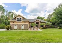Expansive two-story home with a manicured lawn, stone accents, and mature trees on a sunny day at 6720 Winter Garden Vineland Rd, Windermere, FL 34786