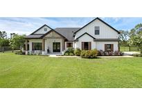 Charming farmhouse exterior with lush lawn, black roof, white siding, and welcoming front porch at 27071 Moss View Dr, Tavares, FL 32778