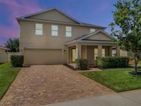 Charming two-story home featuring a brick driveway and manicured front lawn with lush greenery at dusk at 2432 Riviera Ln, Minneola, FL 34715