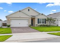 Charming single-story home featuring a well-manicured lawn, brick driveway, and an attached two-car garage at 5808 Arboretum St, St Cloud, FL 34771