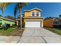 Two-story yellow home featuring a two-car garage and a well-maintained front yard with a mature palm tree at 1129 Royal Ridge Dr, Davenport, FL 33896