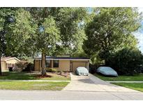 Cozy home with a large, mature tree in the front yard and a covered vehicle in the driveway at 34 W Bob White St, Apopka, FL 32712