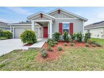 Charming single-story home with a red front door, grey siding, and a well-maintained lawn with tidy landscaping at 584 S Andrea Cir, Haines City, FL 33844