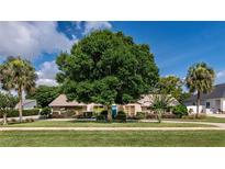 Charming home featuring a lush green lawn and mature trees, including palms, creating a serene outdoor space at 6226 Wynfield Court, Orlando, FL 32819