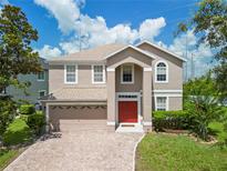 Charming two-story home with red door, beige exterior, manicured lawn and brick driveway at 10142 Serotina Ct, Orlando, FL 32832