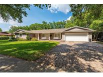 Charming single-story home featuring a manicured lawn, brick driveway, and inviting porch swings at 1111 Pinar Dr, Orlando, FL 32825