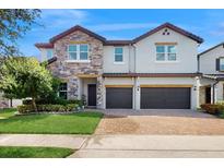 Beautiful two-story home featuring stone accents, manicured lawn, and a brick driveway leading to a three-car garage at 14124 Dove Hollow Dr, Orlando, FL 32824