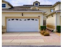 Two-story home featuring a white garage door, manicured landscaping, and a brick walkway at 17322 Chateau Pine Way, Clermont, FL 34711