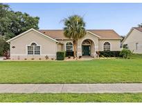 Charming single-story home boasts a lush lawn, manicured landscaping, and a welcoming entrance with a stately palm tree at 14322 Pine Cone Trl, Clermont, FL 34711