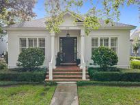 Charming home with a brick staircase leading to a dark wood front door framed by stately columns and lush landscaping at 4545 Fox St, Orlando, FL 32814