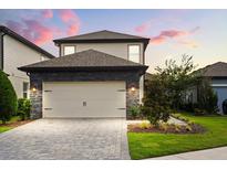 Two-story home with a neutral color palette, stone accents, and a two-car garage, complemented by lush landscaping at 1409 Bellamy Dr, Reunion, FL 34747