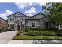 Beautiful two-story home with stone accents, landscaped yard, and a paver driveway under a partly cloudy blue sky at 17551 Black Rail St, Windermere, FL 34786