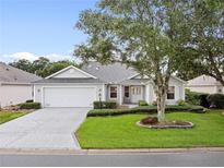 Charming single-story home featuring a well-manicured lawn, mature trees, and a two-car garage at 16950 Se 80Th Bellavista Cir, The Villages, FL 32162