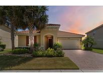 Charming single-story home with a tile roof, lush landscaping, and a brick driveway at sunset at 3906 Carrick Bend Dr, Kissimmee, FL 34746