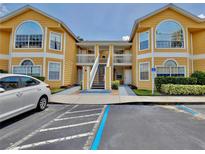Exterior view of a sunny yellow condominium building with two stories and covered walkways to the entrance at 8709 Knightsbridge Ct # B, Kissimmee, FL 34747