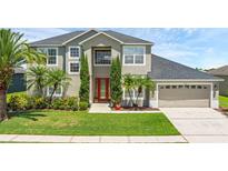 Beautiful two-story home with a well-manicured lawn, red door, and lush landscaping at 3131 Regal Darner Dr, Kissimmee, FL 34744