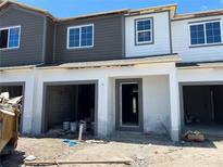 New townhouse construction showing the two-story facade and garage entrance, unfinished yard in front, and a blue sky above at 4224 Campsite Loop, Orlando, FL 32824