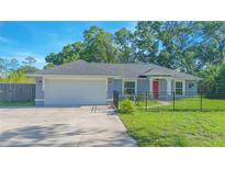 Charming single-story home with a manicured lawn, gray exterior, red door and two-car garage at 4911 Ne 7Th St, Ocala, FL 34470