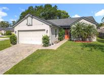 Charming single-story home with a well-manicured lawn, brick driveway, and an inviting orange front door at 1044 Dees Dr, Oviedo, FL 32765