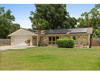 Charming single-story home with stone accents, solar panels, a well-manicured lawn, and mature trees at 12 Horseman Cv, Longwood, FL 32750