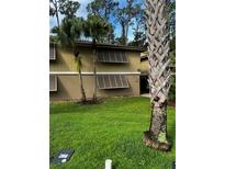 Exterior view of tan two-story building with well-manicured lawn and tropical landscaping at 120 Hibiscus Woods Ct # 11B, Deltona, FL 32725