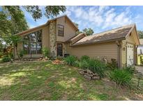 Charming tan home featuring a stone facade, large windows, mature landscaping, and an attached garage at 25438 Pine Valley Dr, Sorrento, FL 32776