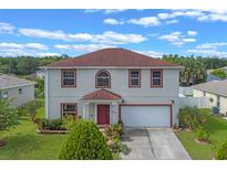 Charming two-story home features red trim, a well-manicured lawn, and an attached two-car garage at 404 Bar Ct, Kissimmee, FL 34759