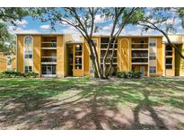 Inviting yellow apartment building with mature trees and well-maintained green lawn under a blue sky at 5263 Images Cir # 306, Kissimmee, FL 34746